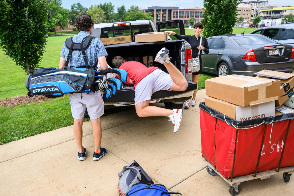 A new student dives headfirst into the back of a pickup truck on move-in day as his parents hold golf clubs and other gear to take into the dorms.