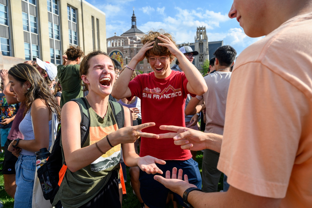 Among a crowd of fellow students, two new UW students both throw scissors in a game of rock-paper-scissors. A third student watches in amused disbelief.