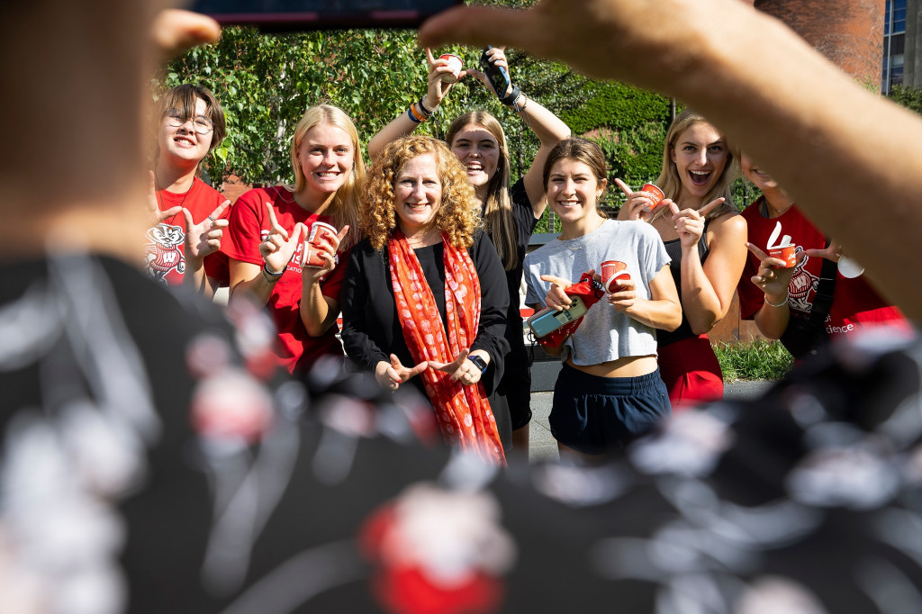 A group of students and Chancellor Jennifer Mnookin make W signs with their thumbs and forefingers while smiling toward the camera.
