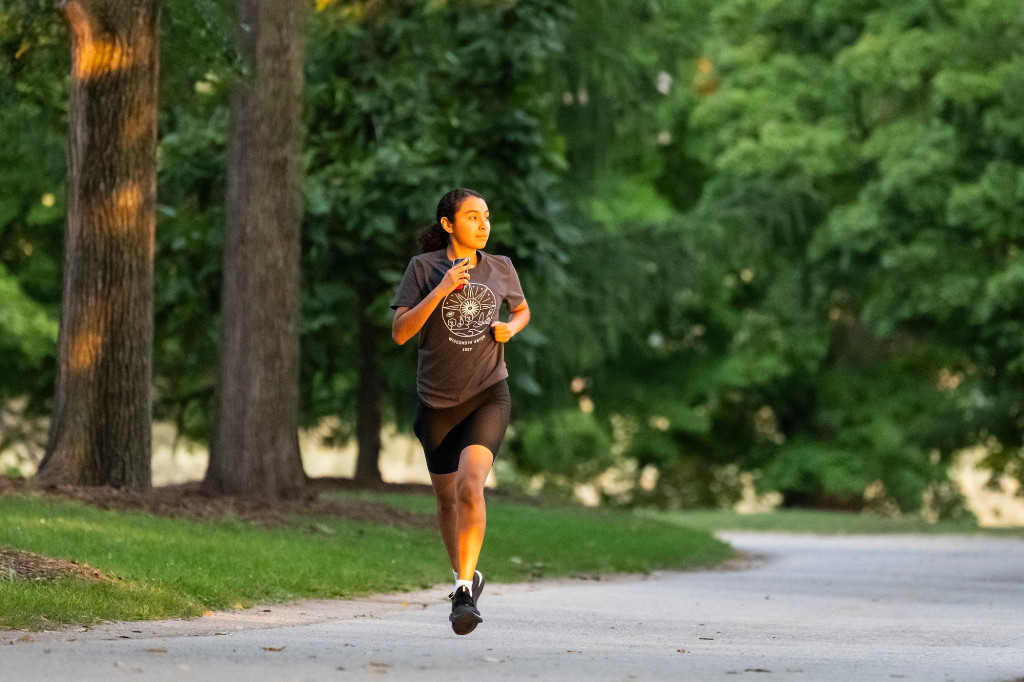 A woman runs down a broad, tree-lined path in the morning light.