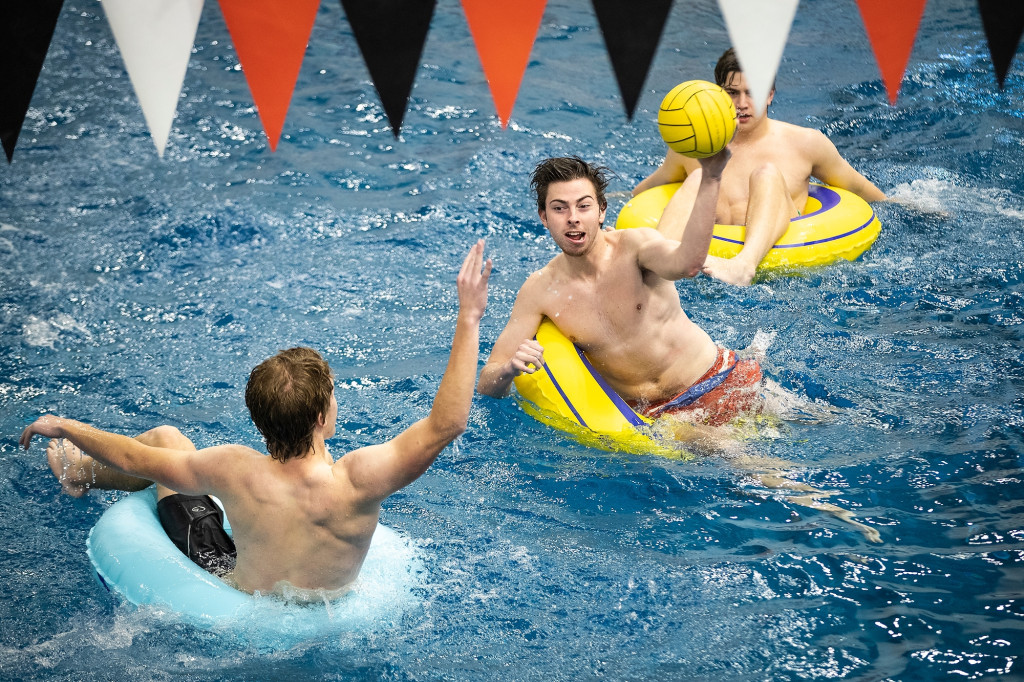 Three students float on inner tubes in the Nick swimming pool. The student in the middle concentrates as he throws a water polo ball past his opponent.