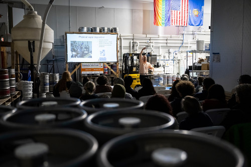 Mark Ediger gestures with his hands as he speaks to an audience among kegs and other supplies in a warehouse setting in the Delta Beer Lab.