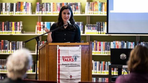 Lori Kido Lopez speaks from apodium in a library setting. A Badger Talks banner hangs from the front of the podium.