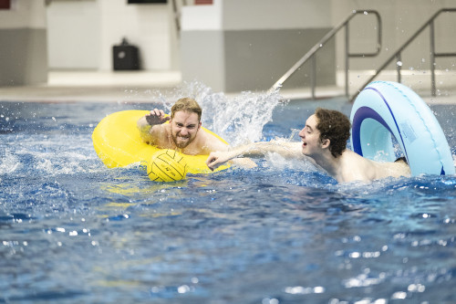 Students from rival inner-tube water polo teams swim towards the ball.