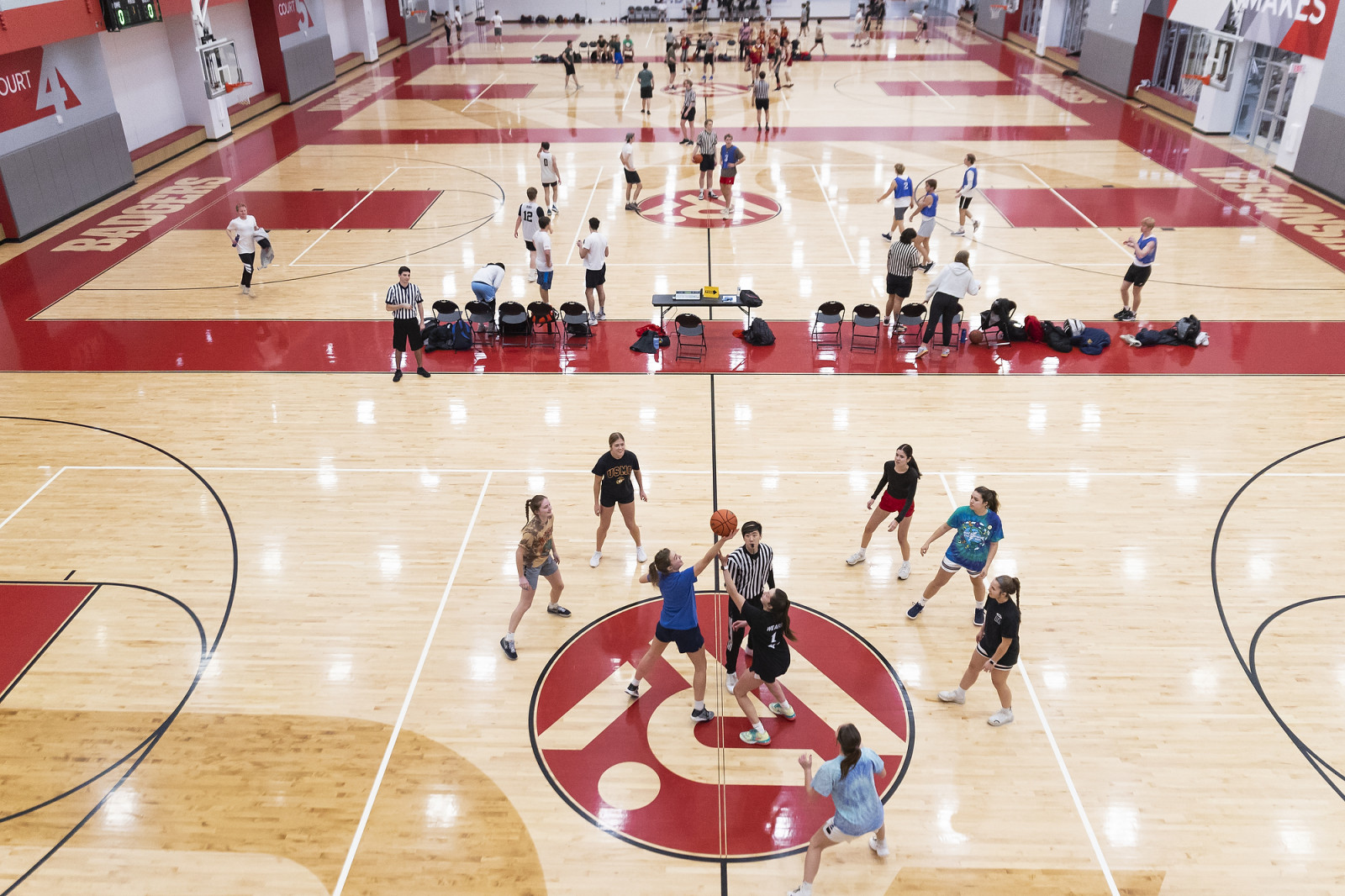 Students in a gym play intramural basketball on four courts