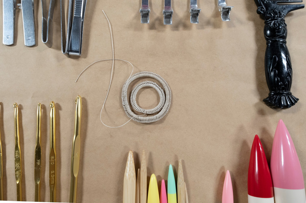 Aerial view of a table displaying knitting needles, crochet hooks and tweezers around a single, crocheted fiberglass loop.