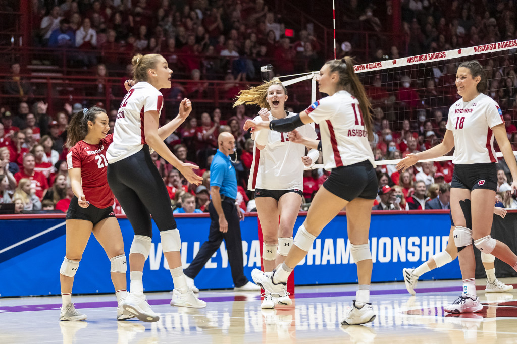 Uniformed volleyball players gather on the court and slap hands.