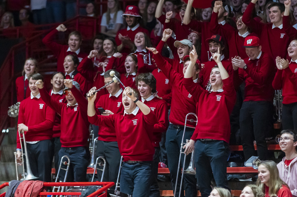 Badgers band members wearing red uniforms shake their fists and shout, while holding instruments.