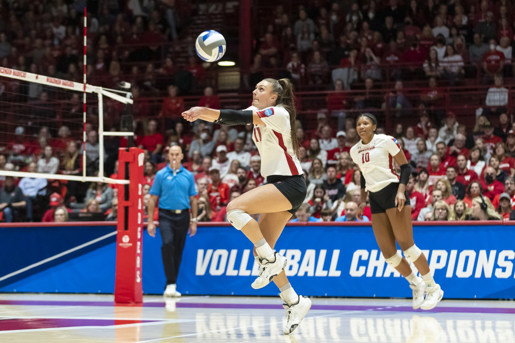 A volleyball player hits the ball as she jumps high.