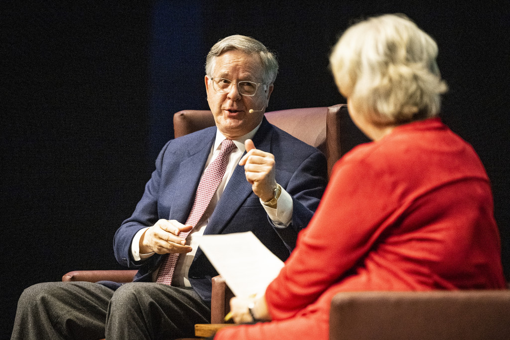 Pete Williams gestures with one hand while speaking on stage to Kathleen Culver.