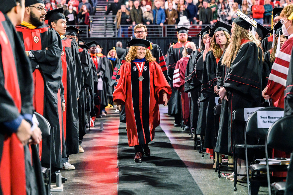 Chancellor Mnookin walks down an aisle amongst a crowd wearing academic regalia from UW–Madison.