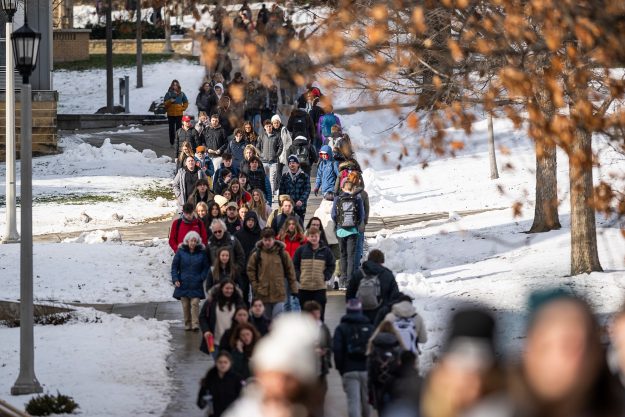 A look at a crowded pedestrian walkway, with snow on the lawns on either side.