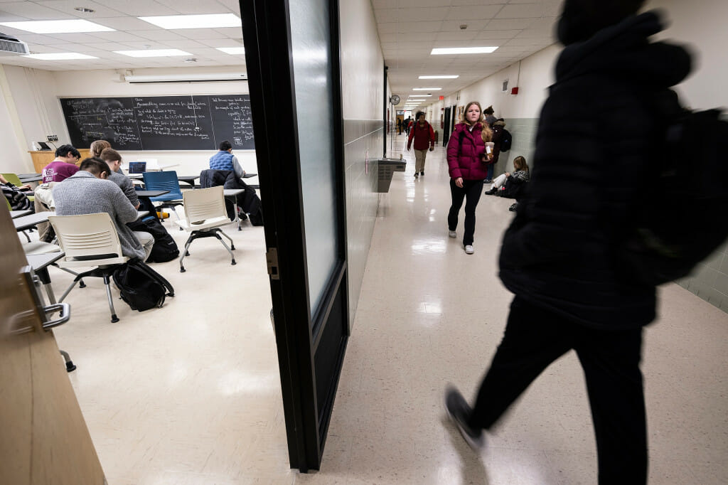 People walk down a hallway, others sit in a nearby classroom.