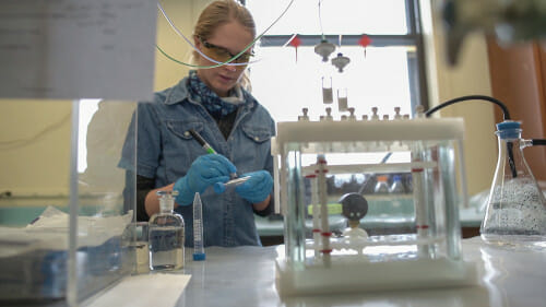 Sarah Balgooyen works in a lab setting wearing protective glasses and gloves.