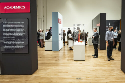 A wide view of the Sifting and Reckoning exhibition with visitors stopping to read materials on display.