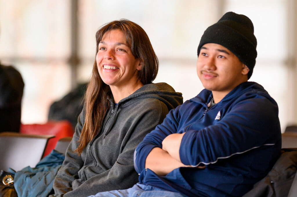 Anna Sherwood (of the Aleut Nation) and her nephew Derek Phi smile as their mentor Wayne Valliere introduces the Ojibwe Winter Games. Sherwood is an Ojibwe Language classroom assistant in the Lac du Flambeau Public School.