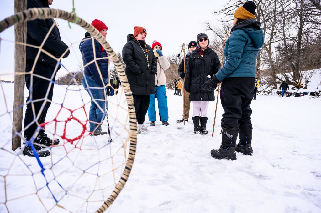 Ann Sherwood, an Ojibwe language assistant at the at the Lac du Flambeau Public School, explains the hoop and spear game (dakobijigan-minawaa zhiimaagan) to participants including several UW students taking second semester Ojibwe.
