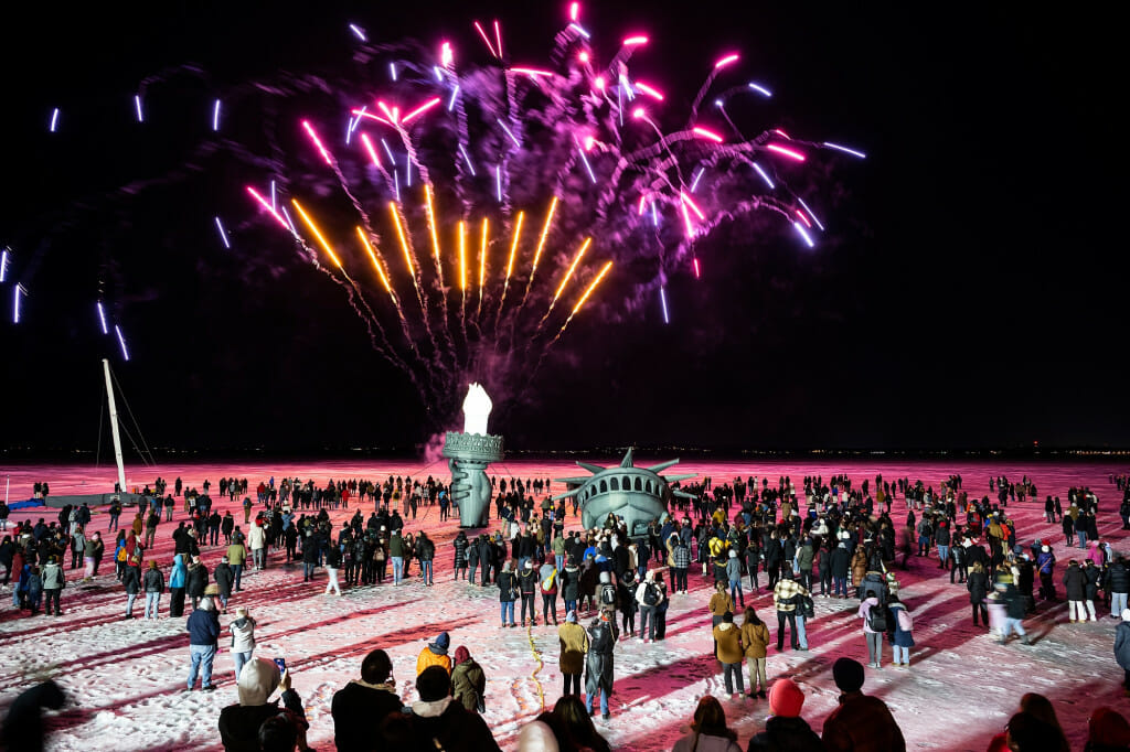 Hundreds of people watch as fireworks light up the night sky above an inflatable replica of the Statue of Liberty’s head, arm and torch on Lake Mendota.