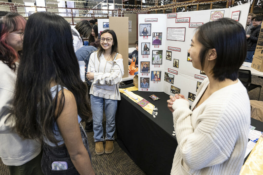Hmong American Student Association officers Hailey Xiong (right) and Elleana Moua (center) talk with students at their information table.
