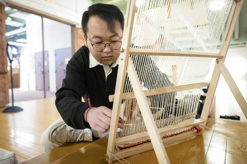 UW alum Chee Meng Xiong uses thread and a loom to take part in a community weaving project.