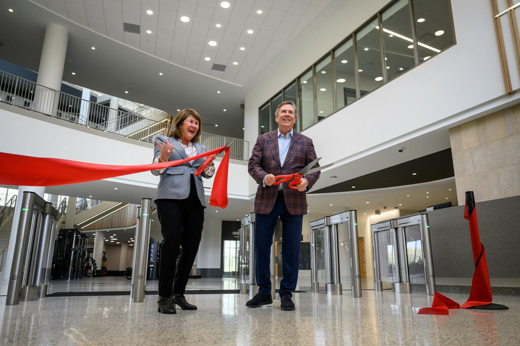 A man and woman stand, smiling, after cutting a big red ribbon.