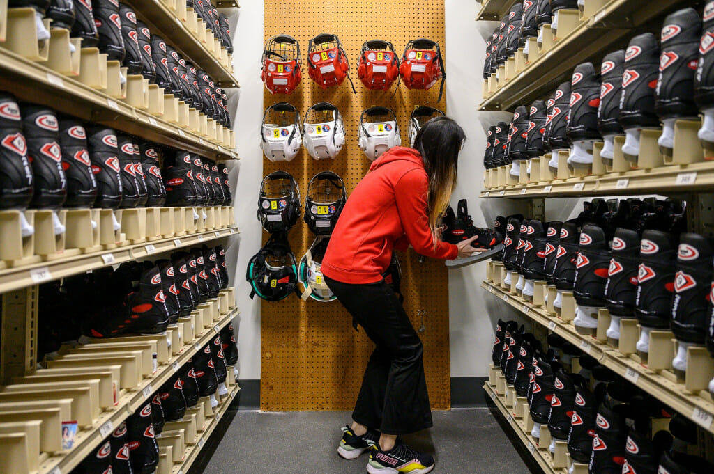 A person puts hockey skates back on a shelf in a room filled with shelves of hockey skates.