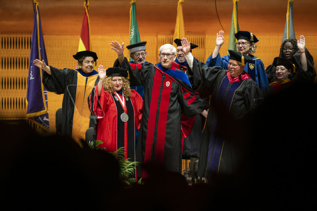 Chancellor Jennifer Mnookin, joined by Gov. Tony Evers to her right and former UW Chancellors Donna Shalala, David Ward and Jon Wiley behind her, join the audience in singing Varsity.