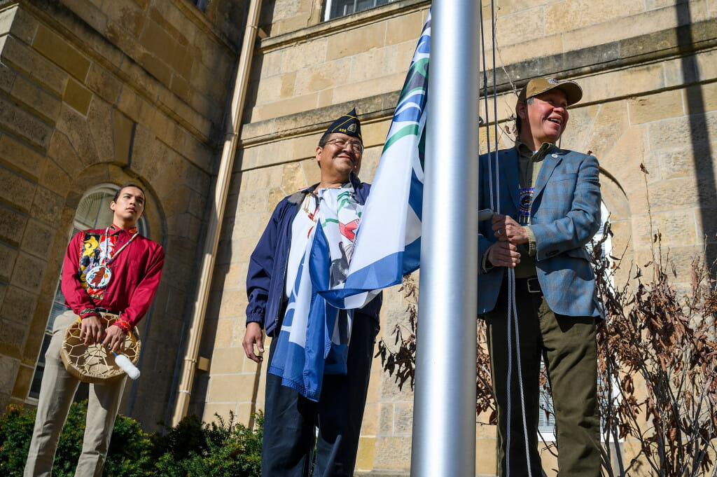 From left to right, Cordell Funmaker, Ho-Chunk Nation tribal member; Marcus WhiteEagle, Ho-Chunk marine veteran; and Marlon WhiteEagle, president of the Ho-Chunk Nation and marine veteran; prepare to raise the Ho-Chunk Nation’s flag in front of Bascom Hall on a sunny day.