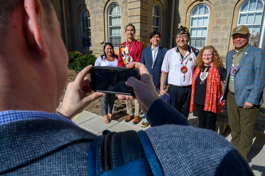 From left to right, Carla Vigue, tribal relations director in the Office of University Relations at the UW; Cordell Funmaker, Ho-Chunk Nation tribal member; Casey Brown, public relations officer with the Ho-Chunk Nation; Marcus WhiteEagle, Ho-Chunk marine veteran; Chancellor Jennifer Mnookin; and Marlon WhiteEagle, president of the Ho-Chunk Nation and marine veteran; stand for a portrait by Ho-Chunk Nation member Ryan Greendeer after the raising of the Ho-Chunk Nation’s flag in front of Bascom Hall on a sunny day.