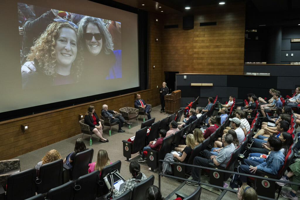 A lecture hall full of people look at a photo of two women on the big screen.
