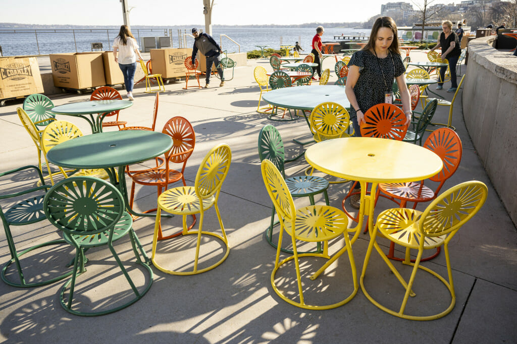 Ashley Alloway places a metal chair at a yellow table on the Memorial Union Terrace.