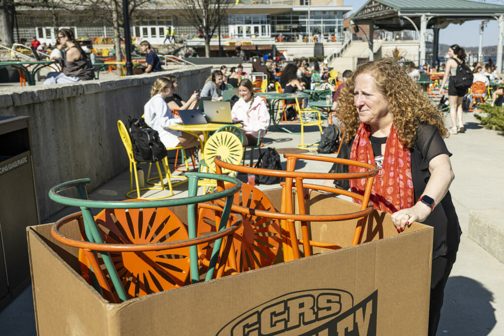 Jennifer Mnookin pushes a trolly loaded with metal chairs across a sunny, crowded Memorial Union Terrace.