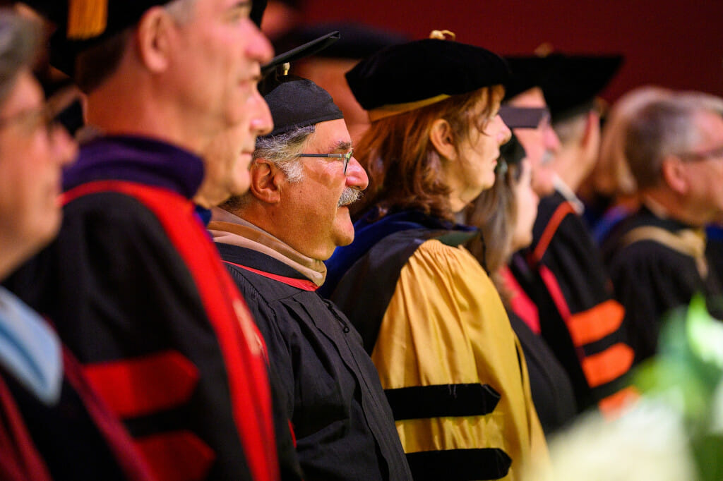 A line of people stand on stage wearing academic regalia.