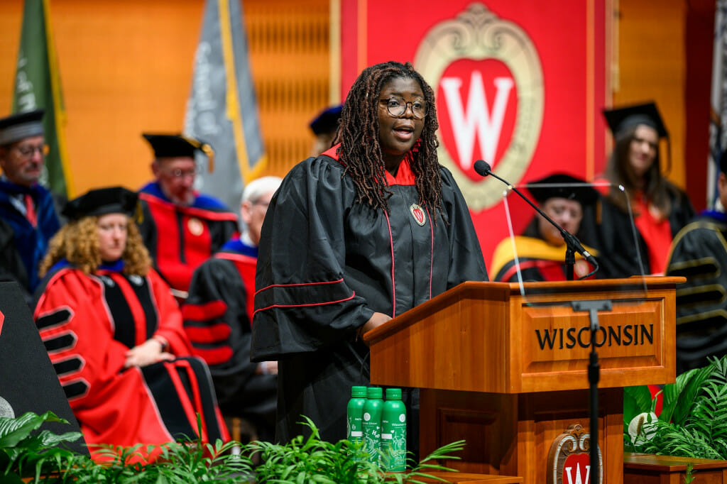 A woman wearing academic robes speaks at a lectern.
