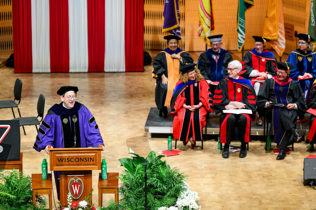 People laugh as a man wearing doctoral robes and hat speaks on stage.