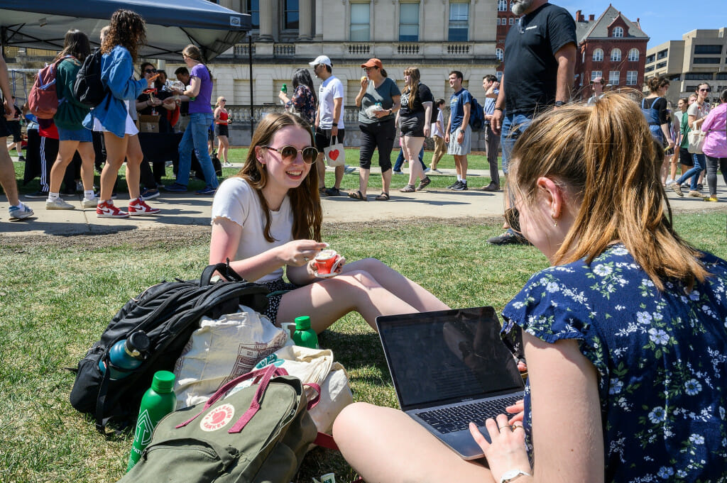 Two women sit on the grass and eat ice cream.