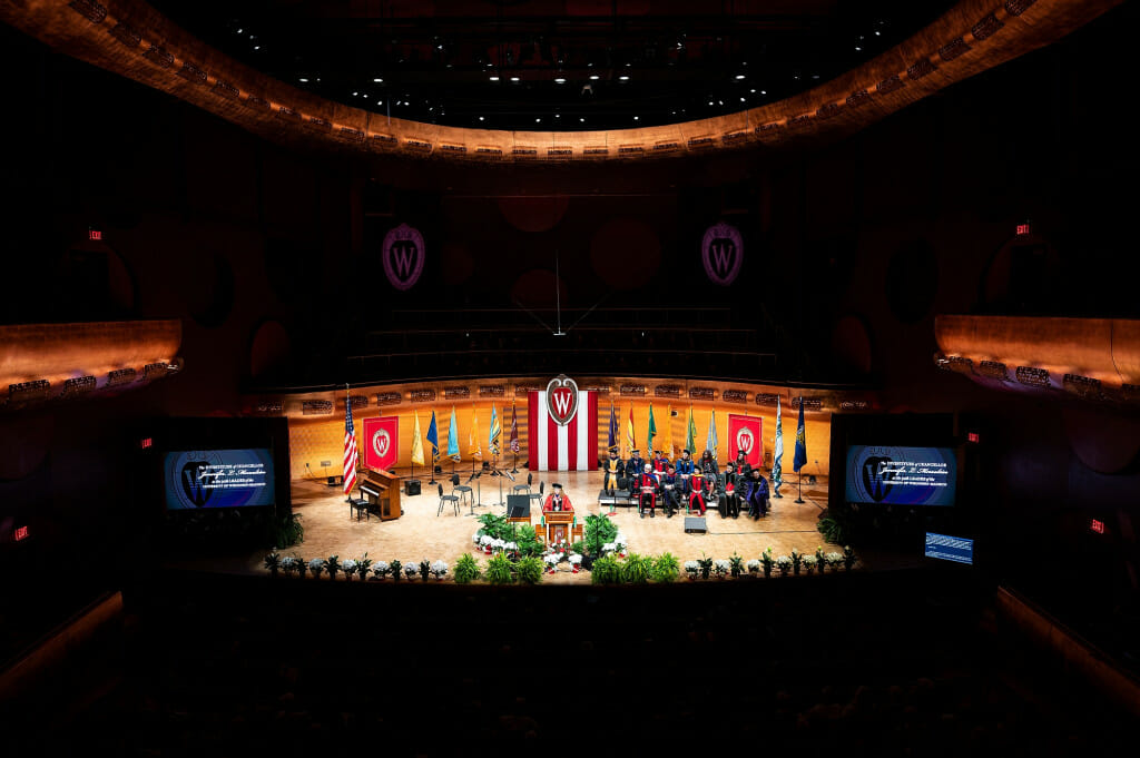 A concert hall is shown, filled with people attending the investiture ceremony.