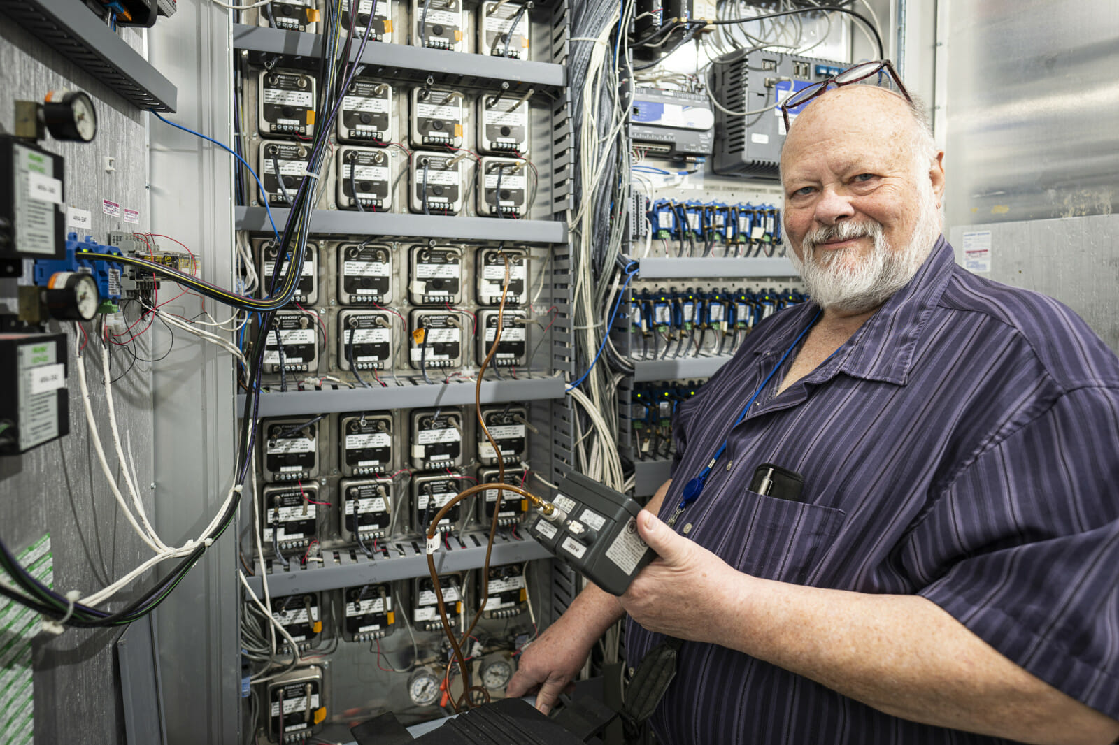 A man stands in front of a piece of equipment with wires sticking out of it.