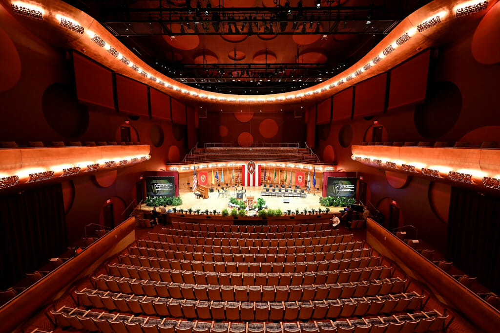 View of empty theater with a stage decorated in red and white with a UW–Madison crest. 