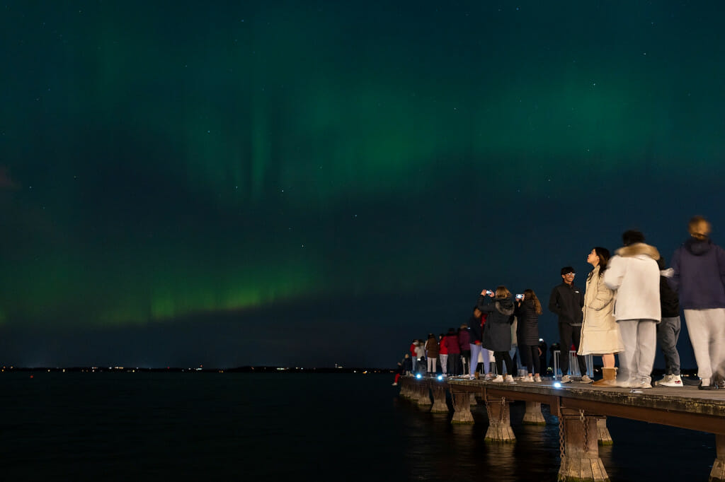 Students line a pier jutting out into the lake as the Northern Lights sparkle.