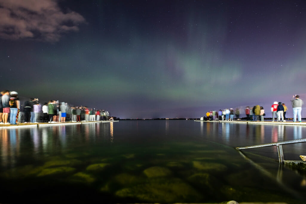 Students fill two piers jutting out into the lake as the Northern Lights sparkle.