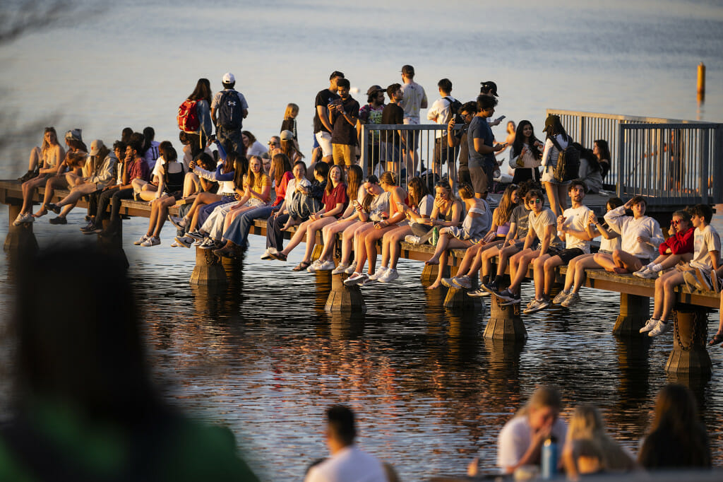 A crowd of people sit and stand on a pier over a lake.