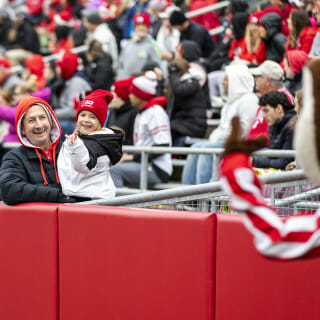 A woman and a young child wave from the stands at Camp Randall.