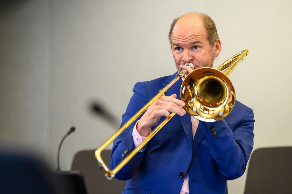 A man in a bright blue suit coat plays the trombone