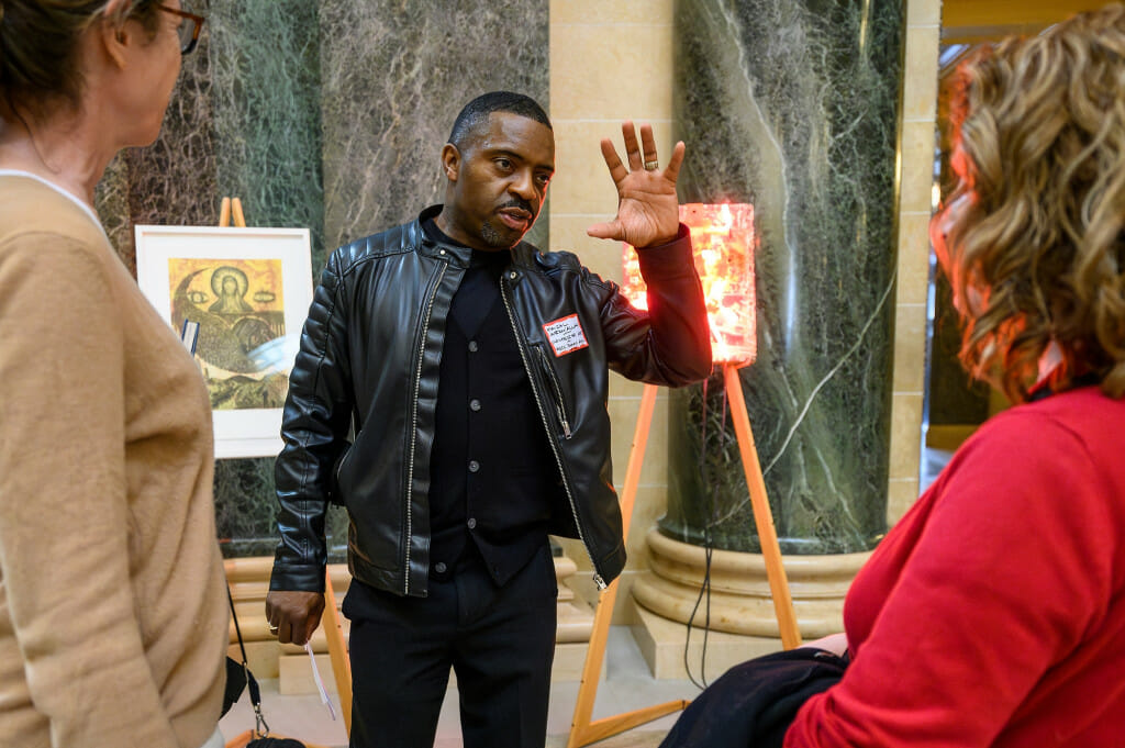 A man raises one hand to gesture as he talks about his research while standing in the Wisconsin Capitol rotunda.