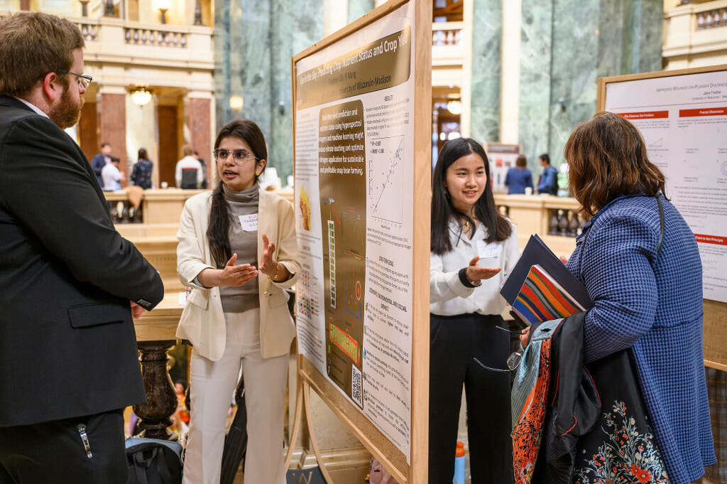In the Wisconsin Capitol rotunda, two women stand on either side of a large research poster display