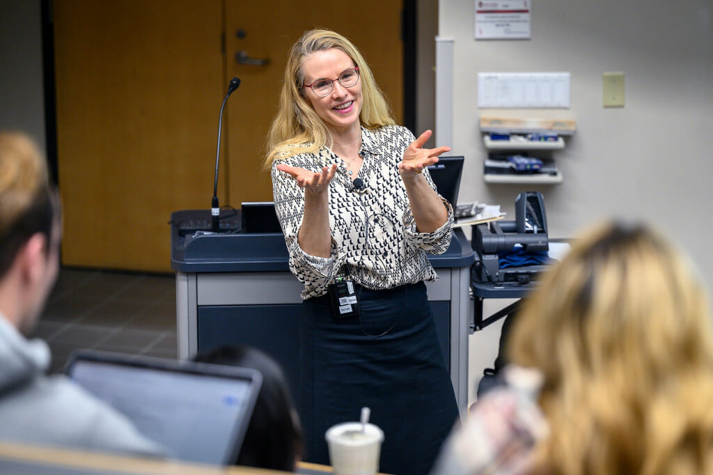 A woman gestures as she talks to a room of students.