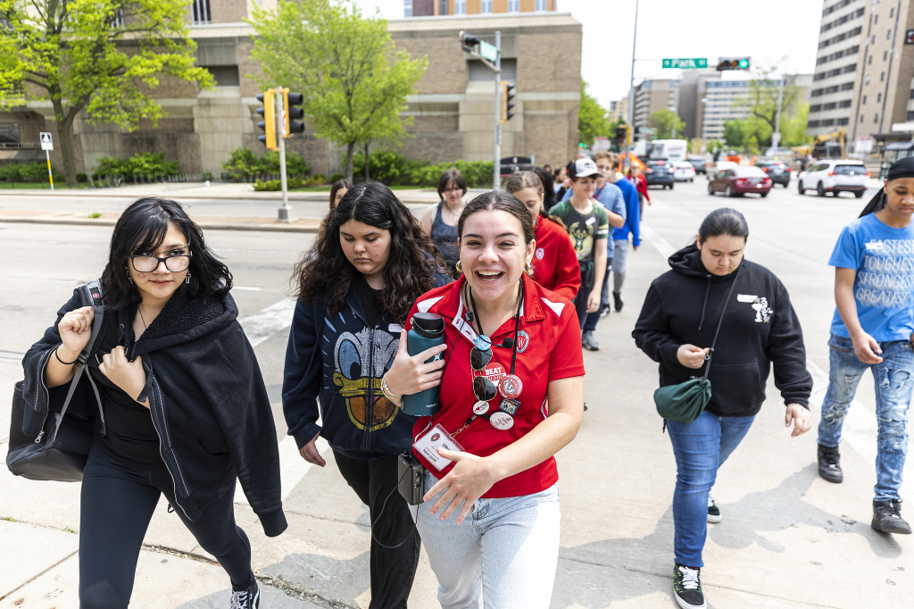 A woman wearing red and white leads a group of children down a street.