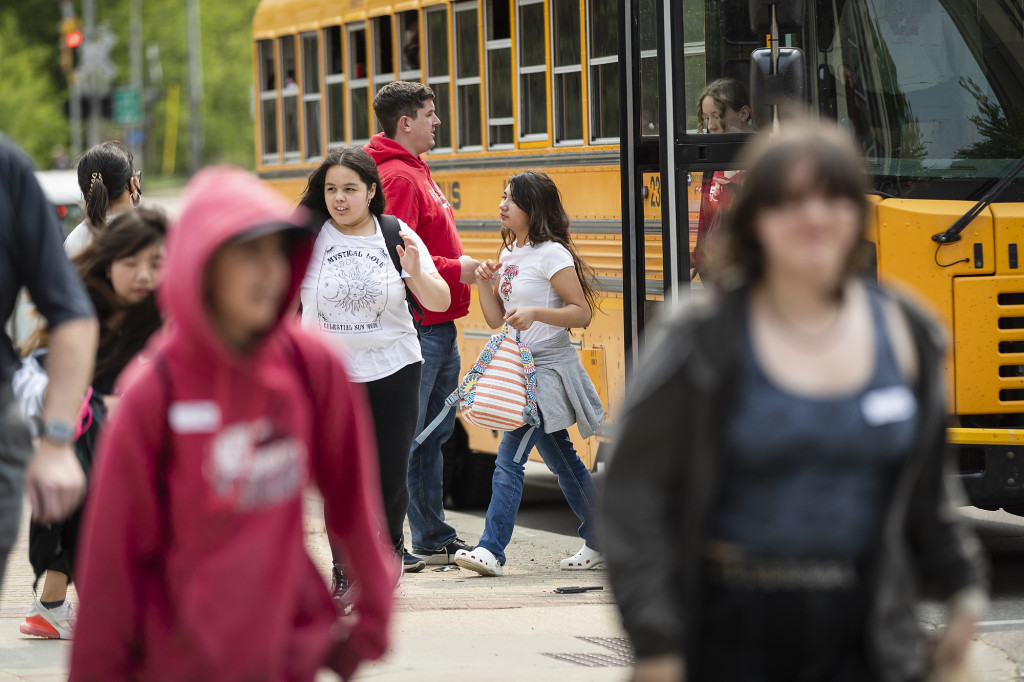 Students get off a bus, one fist-bumps a teacher.