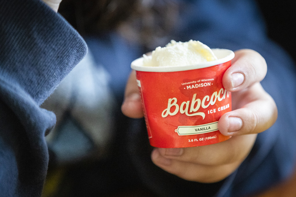 A hand holds a cup of ice cream, the cup reads "Babcock Ice Cream."